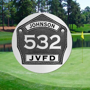May include: A silver round metal sign with a black and white firefighter patch. The patch has the name "JOHNSON" at the top, the number "532" in the center, and the letters "JVFD" at the bottom.