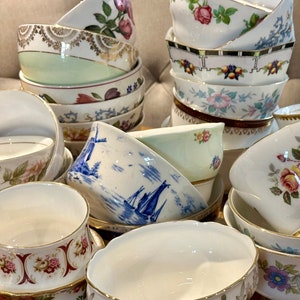 Puede incluir: Una colección de tazas de té y platillos vintage en varios patrones florales. Las tazas están apiladas y dispuestas en forma de pirámide, con la taza más grande en la parte inferior y la taza más pequeña en la parte superior. Las tazas están hechas de porcelana blanca y tienen ribetes dorados. Los patrones florales son en tonos de rosa, azul y verde.