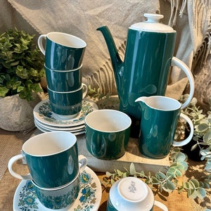 May include: A vintage green and white tea set with floral patterns on the saucers. The set includes a teapot, creamer, sugar bowl, and four cups.