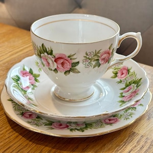 Könnte beinhalten: Ein weißes Tee-Set mit einem Blumenmuster aus rosa Rosen und grünen Blättern. Das Set hat einen goldenen Rand.