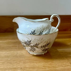 Peut inclure: Un ensemble de crémier et de sucrier en céramique blanche avec un motif de feuilles vertes et dorées.