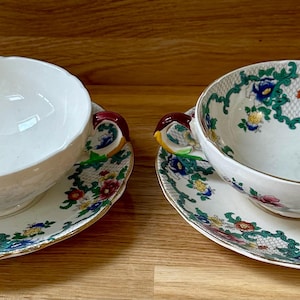 May include: Two vintage floral soup bowls with matching saucers. The bowls have a white background with a green, red, and yellow floral pattern. The saucers have a similar pattern.