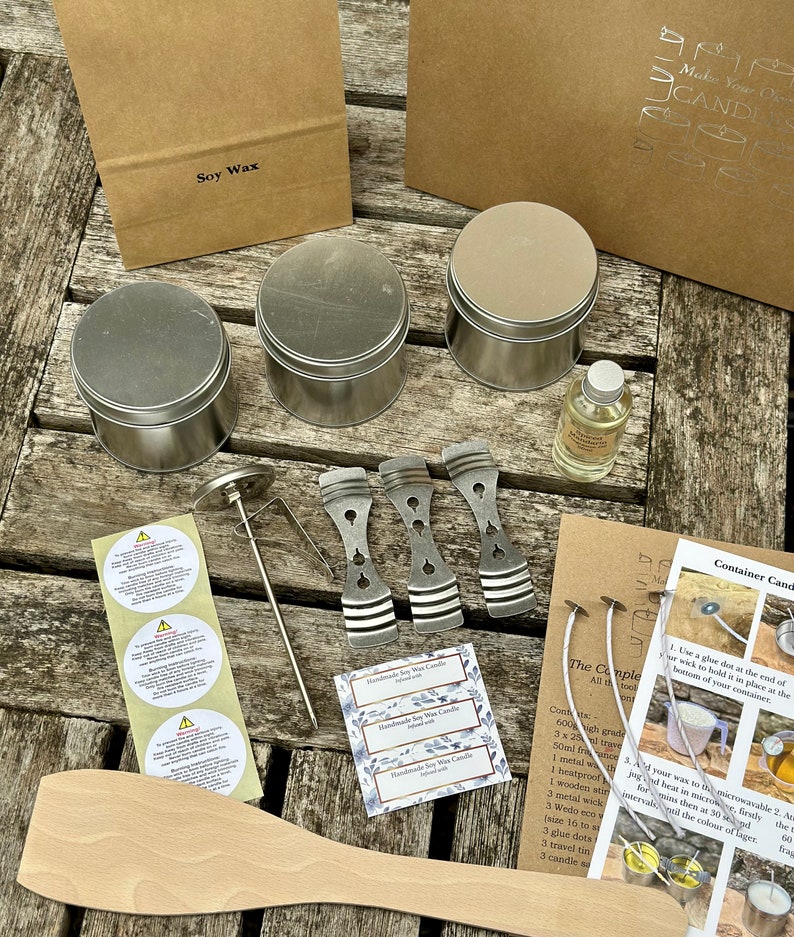 May include: A candle-making kit with various supplies, including soy wax, metal tins, a thermometer, wicks, and a wooden stirring spoon. The kit also includes labels and instructions for making container candles. The kit is arranged on a wooden surface.