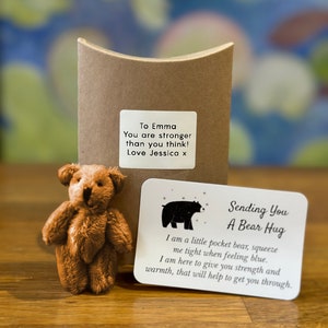 Può includere: Un piccolo orsacchiotto di peluche marrone con un biglietto che dice "Sending You A Bear Hug" e include il testo "Sono un piccolo orsacchiotto tascabile, stringimi forte quando ti senti giù. Sono qui per darti forza e calore, che ti aiuteranno a superare questo momento."