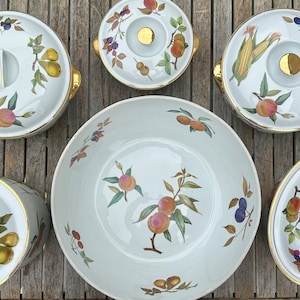 May include: A set of five white porcelain serving dishes with gold trim and a fruit and floral design. The dishes feature a variety of fruits, including peaches, pears, and plums, as well as green leaves and flowers. The dishes are perfect for serving a variety of foods, from appetizers to desserts.
