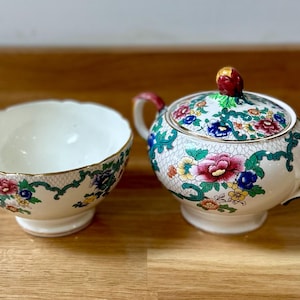 May include: A vintage floral patterned sugar bowl and creamer set. The sugar bowl has a lid with a floral design and a gold trim. The creamer is a small bowl with a floral design and a gold trim.