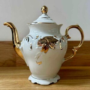 Puede incluir: Tetera de porcelana blanca con detalles dorados. La tetera presenta un pico y asa curvos, una tapa decorativa y diseños de hojas doradas. Un diseño clásico, adecuado para servir té.