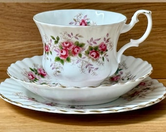 Peut inclure: Service à thé blanc avec une tasse, une soucoupe et une assiette. L'ensemble présente un motif floral de roses roses et de feuilles vertes. Les bords sont festonnés et garnis d'or.