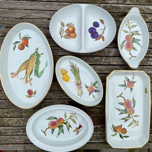May include: A selection of white ceramic serving platters with gold rims. Each platter features a different hand-painted design of fruits and vegetables, including peaches, plums, corn, and asparagus.