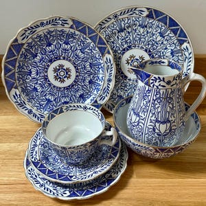 Puede incluir: Un juego de té de porcelana azul y blanca con un diseño floral. El juego incluye platos, una jarra, un cuenco y una taza de té con un platillo. Los bordes de los platos y la taza de té son festoneados. El juego tiene ribete dorado.
