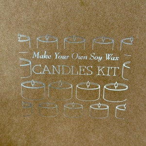 May include: A brown paper kit with silver line drawings of candles. The text "Make Your Own Soy Wax CANDLES KIT" is printed in silver. The image features multiple candle illustrations.