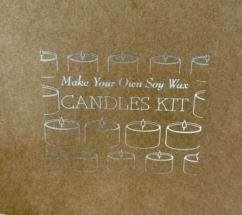 May include: A brown paper kit with silver line drawings of candles. The text "Make Your Own Soy Wax CANDLES KIT" is printed in silver. The image features multiple candle illustrations.