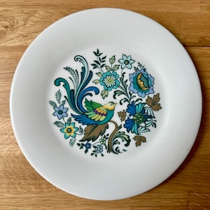 May include: White ceramic plate with a colourful bird and floral design. The bird features blue, yellow, and green feathers, perched on a brown branch. The floral pattern includes blue, teal, and yellow flowers.