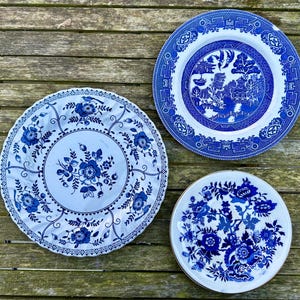 Op de afbeelding: Drie blauwe en witte porseleinen borden met bloem- en geometrische patronen. De borden liggen op een houten oppervlak.