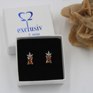 Könnte beinhalten: Ein Paar goldene und silberne Ohrringe mit einem Kronendesign. Die Ohrringe befinden sich in einer weißen Schachtel mit dem Text "exclusiv for you".