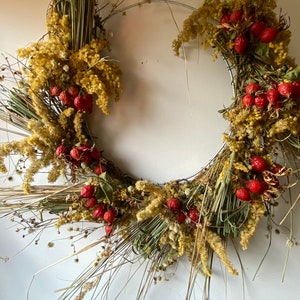 May include: A dried floral wreath with a wire frame, featuring dried grasses, yellow flowers, and red berries.