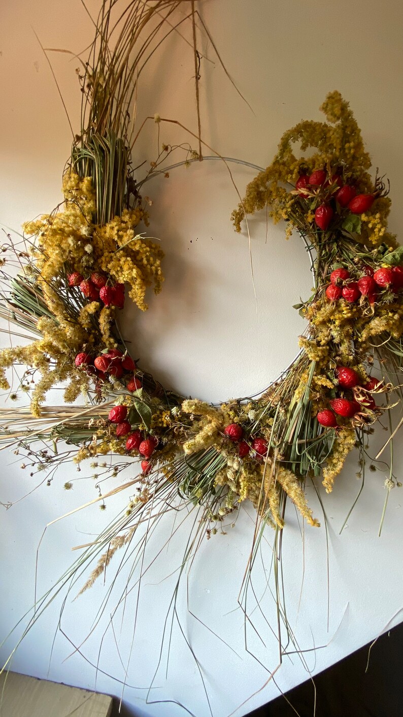May include: A dried floral wreath with a wire frame, featuring dried grasses, yellow flowers, and red berries.