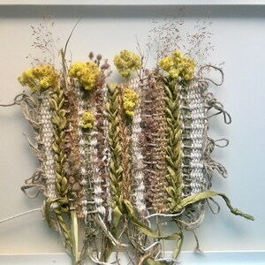 K&ouml;nnte beinhalten: Ein gerahmtes Wandbild mit einer gewebten Tapisserie mit getrockneten Blumen und Pflanzen in Gr&uuml;n- und Gelbt&ouml;nen.