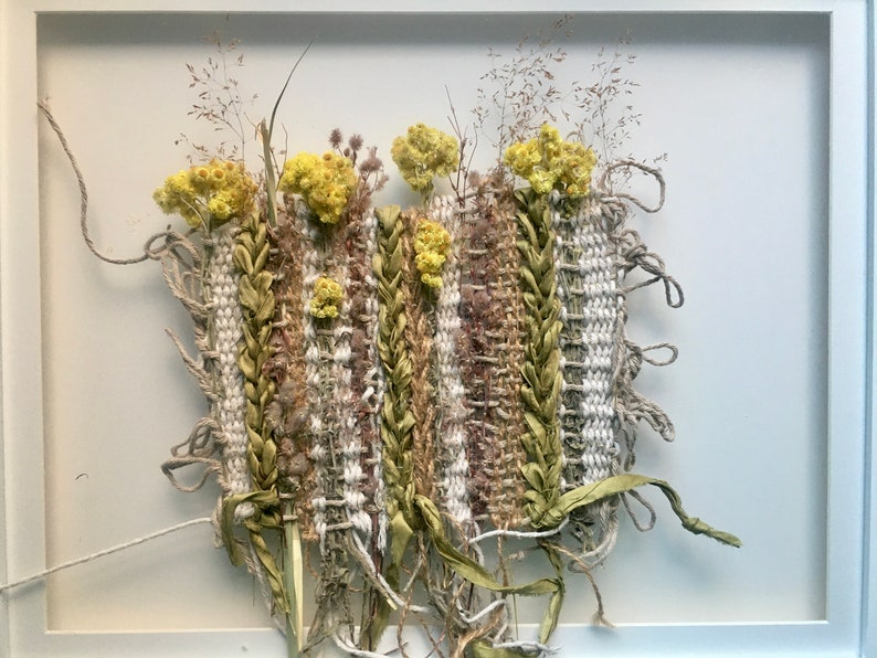 K&ouml;nnte beinhalten: Ein gerahmtes Wandbild mit einer gewebten Tapisserie mit getrockneten Blumen und Pflanzen in Gr&uuml;n- und Gelbt&ouml;nen.