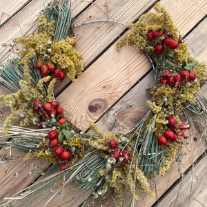 May include: A dried floral wreath with a wire frame, featuring dried grasses, yellow flowers, and red berries.