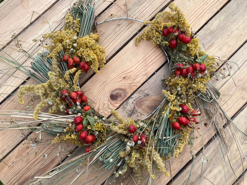 May include: A dried floral wreath with a wire frame, featuring dried grasses, yellow flowers, and red berries.