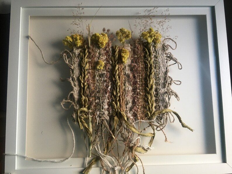 K&ouml;nnte beinhalten: Ein gerahmter Wandbehang mit einer gewebten Tapisserie mit getrockneten Blumen und Gr&auml;sern in Braun-, Beige- und Gelbt&ouml;nen.