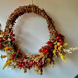 May include: A brown twig wreath decorated with dried flowers and red berries.