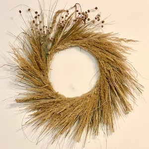 May include: A natural-toned wreath made of dried grasses and flowers. The wreath is circular and has a rustic, bohemian style.