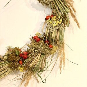May include: A dried floral wreath made with dried grasses, flowers, and berries. The wreath is a natural brown color with pops of red berries and yellow flowers.