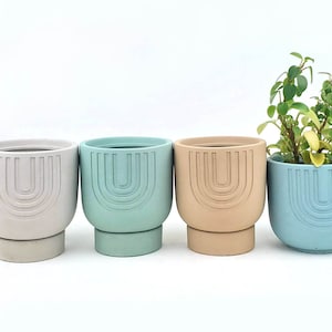 May include: Four ceramic planters with a geometric design. The planters are in white, light blue, beige, and blue. The planters have a rounded base and a slightly flared top. One planter has a small green plant inside.
