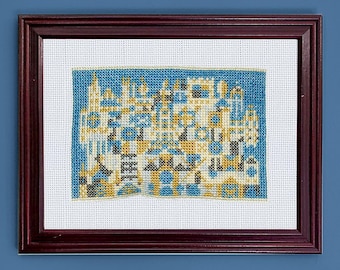 May include: A framed cross-stitch artwork depicting a colorful cityscape with a blue sky background.