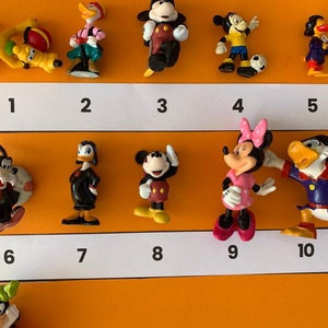 K&ouml;nnte beinhalten: Zehn kleine Plastikfiguren von Disney-Charakteren, darunter Mickey Mouse, Minnie Mouse, Donald Duck, Goofy und Pluto. Die Figuren sind von 1 bis 10 nummeriert.