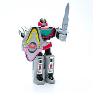 Könnte beinhalten: Rote, schwarze und silberne Roboter-Actionfigur mit Schild und Schwert. Der Roboter hat einen roten Kopf, eine grüne Brust und graue Beine. Der Schild ist grau, gelb und rosa. Das Schwert ist grau.
