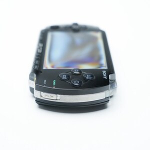 May include: Black Sony PSP handheld game console. The device has a screen, directional buttons, and action buttons. The console has a silver trim and the Sony logo is visible.