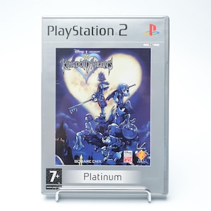 Puede incluir: Caja de videojuego de PlayStation 2 para Kingdom Hearts. La portada presenta personajes en una combinación de colores azul y morado sobre un fondo iluminado por la luna. La caja es plateada con el logotipo de PlayStation 2 en la parte superior y la palabra "Platinum" en la parte inferior.