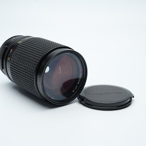 Può includere: Un obiettivo teleobiettivo Tokina AT-X 100-300 mm f/4-5.6 nero con un tappo dell'obiettivo nero.