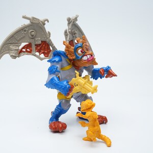 May include: A blue and gray action figure with wings and a gun, standing next to a smaller yellow action figure. Both figures are from the Teenage Mutant Ninja Turtles toy line.