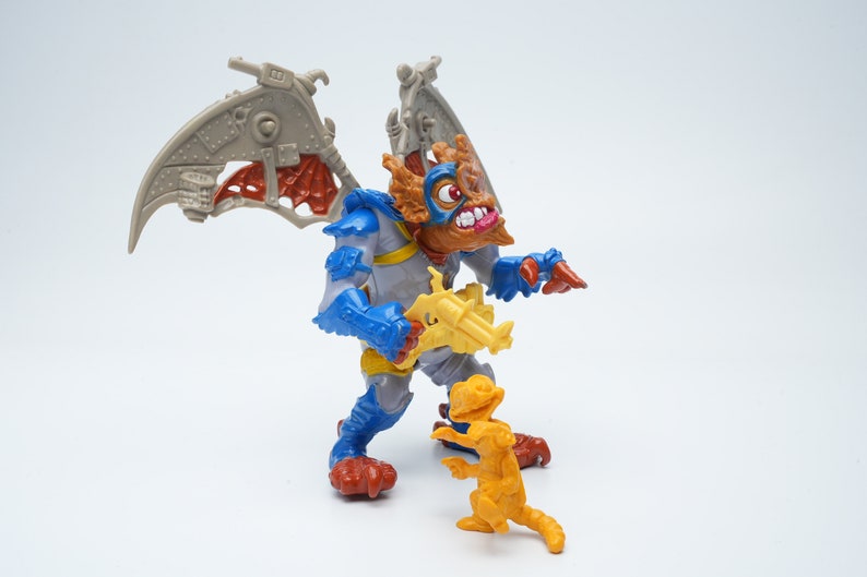 May include: A blue and gray action figure with wings and a gun, standing next to a smaller yellow action figure. Both figures are from the Teenage Mutant Ninja Turtles toy line.