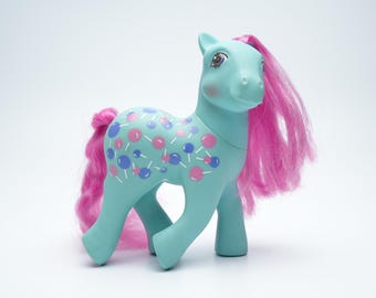Puede incluir: Un pony azul turquesa con pelo rosa y un diseño de piruletas azules y rosas en su cuerpo.