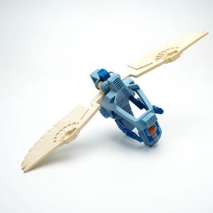 May include: A blue and white plastic toy spaceship with wings. The spaceship has a cockpit and a small orange detail on the front.