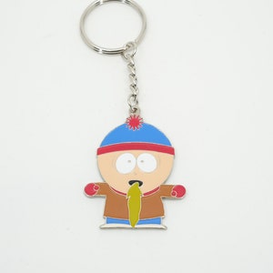 K&ouml;nnte beinhalten: Ein Metall-Schl&uuml;sselanh&auml;nger mit einer Cartoonfigur mit blauem Hut, rotem Rand und brauner Jacke. Die Figur hat einen &uuml;berraschten Gesichtsausdruck und eine gr&uuml;ne Substanz kommt aus ihrem Mund. Der Schl&uuml;sselanh&auml;nger hat eine silberne Kette und einen Ring.