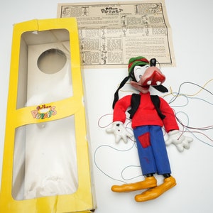 Peut inclure: Une marionnette vintage de Goofy avec une chemise rouge, un pantalon bleu et un chapeau vert. La marionnette est dans sa boîte d'origine avec des instructions d'utilisation. La marionnette est en feutre et possède un système de contrôle par cordes.