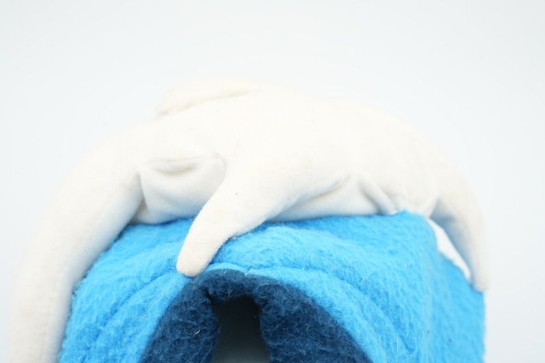Puede incluir: Un juguete de peluche blanco con forma de delf&iacute;n, acostado sobre una superficie de felpa azul y azul oscuro.