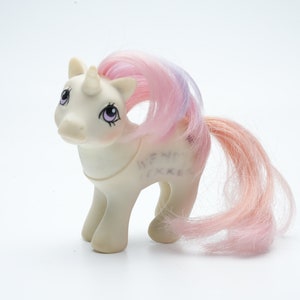 May include: A white unicorn toy with a pink and purple mane and tail. The unicorn has a horn and closed eyes. The toy has writing on its side that says "My Little Pony".