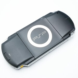 May include: A black handheld PSP game console with a white PSP logo in the center. The console is angled slightly, showing the top and front. The background is plain white.