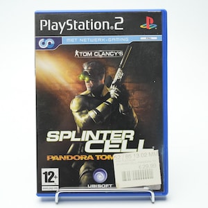 May include: A PlayStation 2 game case with a blue border. The cover features a man holding a gun, with the title "SPLINTER CELL" and "TOM CLANCY'S" visible. The game is rated 12+.