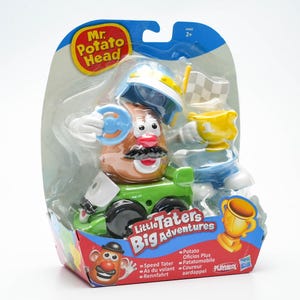 Könnte beinhalten: Ein Mr. Potato Head Spielzeug in einem grünen Rennwagen mit einem blau-weißen Helm, einer gelben Trophäe und einer karierten Flagge. Die Verpackung lautet "Little Taters Big Adventures".