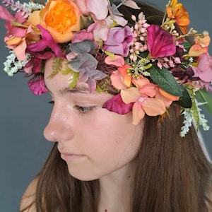 May include: A floral crown with pink, orange, and burgundy flowers. The crown is made of silk flowers and greenery.