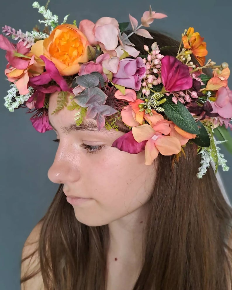 May include: A floral crown with pink, orange, and burgundy flowers. The crown is made of silk flowers and greenery.