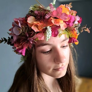 May include: A floral crown with pink, orange, and green flowers. The crown is worn on the head of a person with long brown hair.